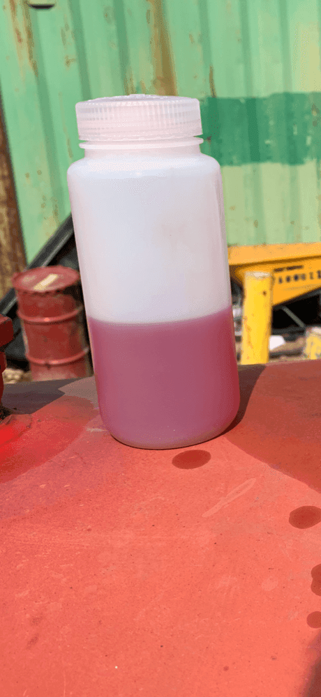 Diesel fuel sample showing a milky, water-hazed layer on top and settled pink-tinted sediment at the bottom